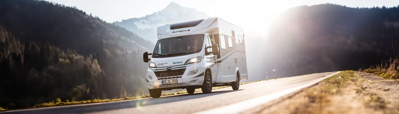 White RV driving on a scenic mountain road at sunrise